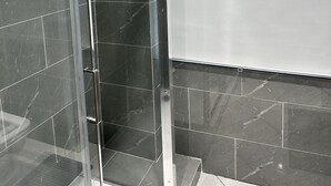 Une salle de bain moderne avec des murs recouverts de carreaux foncés, une douche en verre et un sol carrelé de blanc.