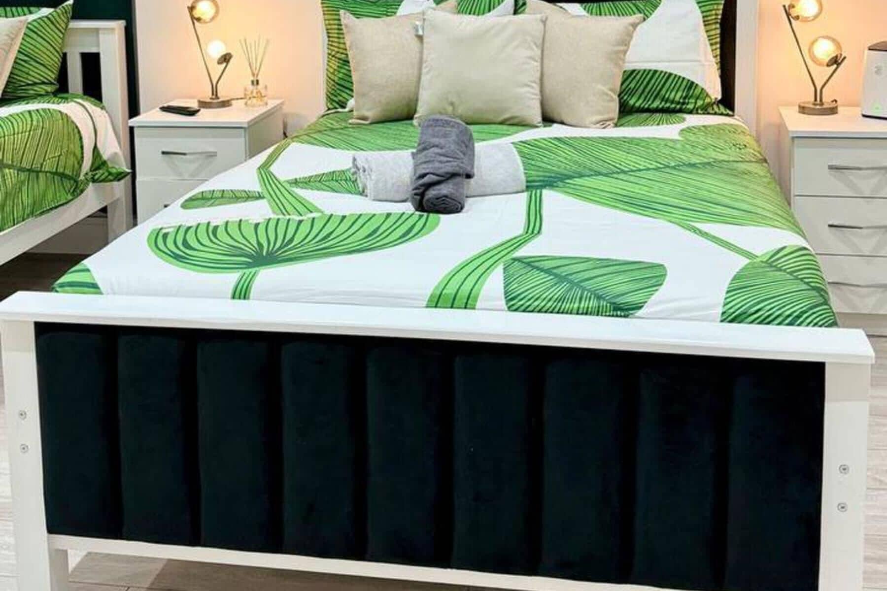 A bed with a green leaf pattern bedspread, white pillows, and a dark headboard.