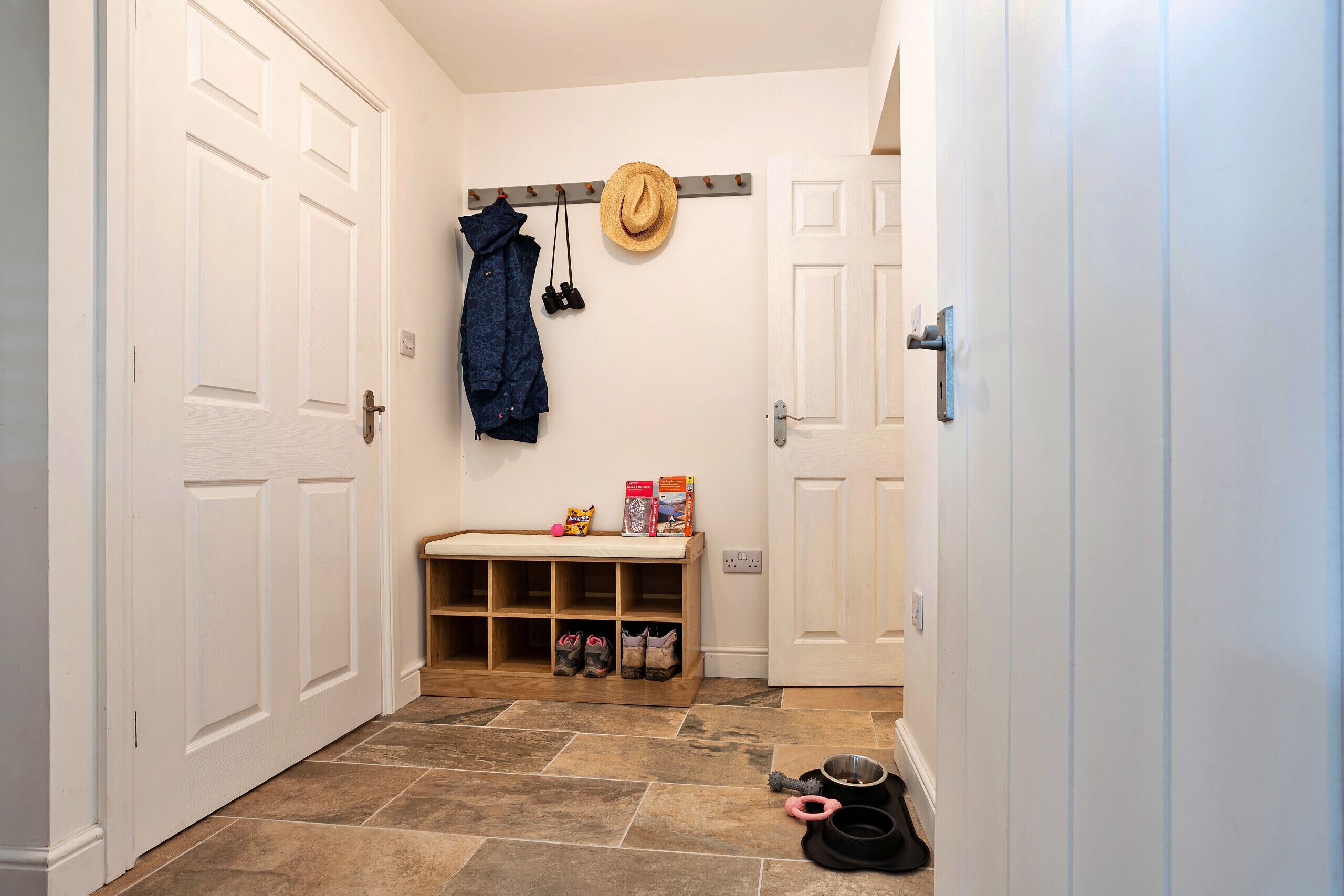 A hallway with a bench, a coat rack with a hat, and a shoe rack with shoes and pet bowls.
