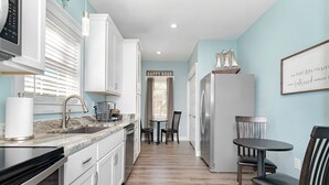 A modern kitchen with white cabinets, a marble countertop, and a built-in oven. There is a dining area with a table and chairs, and a refrigerator. - Deltaville 2BR Retreat, Walk to Museum, Boat Parking (Deltaville)