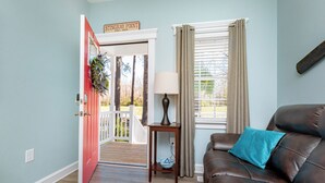 A living room with a brown leather sofa, a small wooden side table, a lamp, and a window with beige curtains. - Deltaville 2BR Retreat, Walk to Museum, Boat Parking (Deltaville)