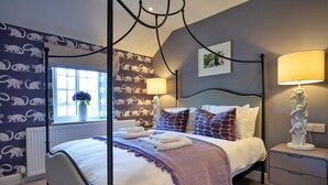 Un lit à baldaquin avec une couvre-lit blanche et violette, deux lampes de chevet et une table de chevet avec une lampe.