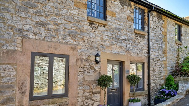Un bâtiment en pierre avec une porte sombre, des fenêtres et des plantes en pot.