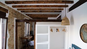 A room with exposed wooden beams, a bed with a blue headboard, a wicker hanging light fixture, and a white shelving unit with clothes. - Elegante Apartamento Frente al Puerto de Denia (Dénia)