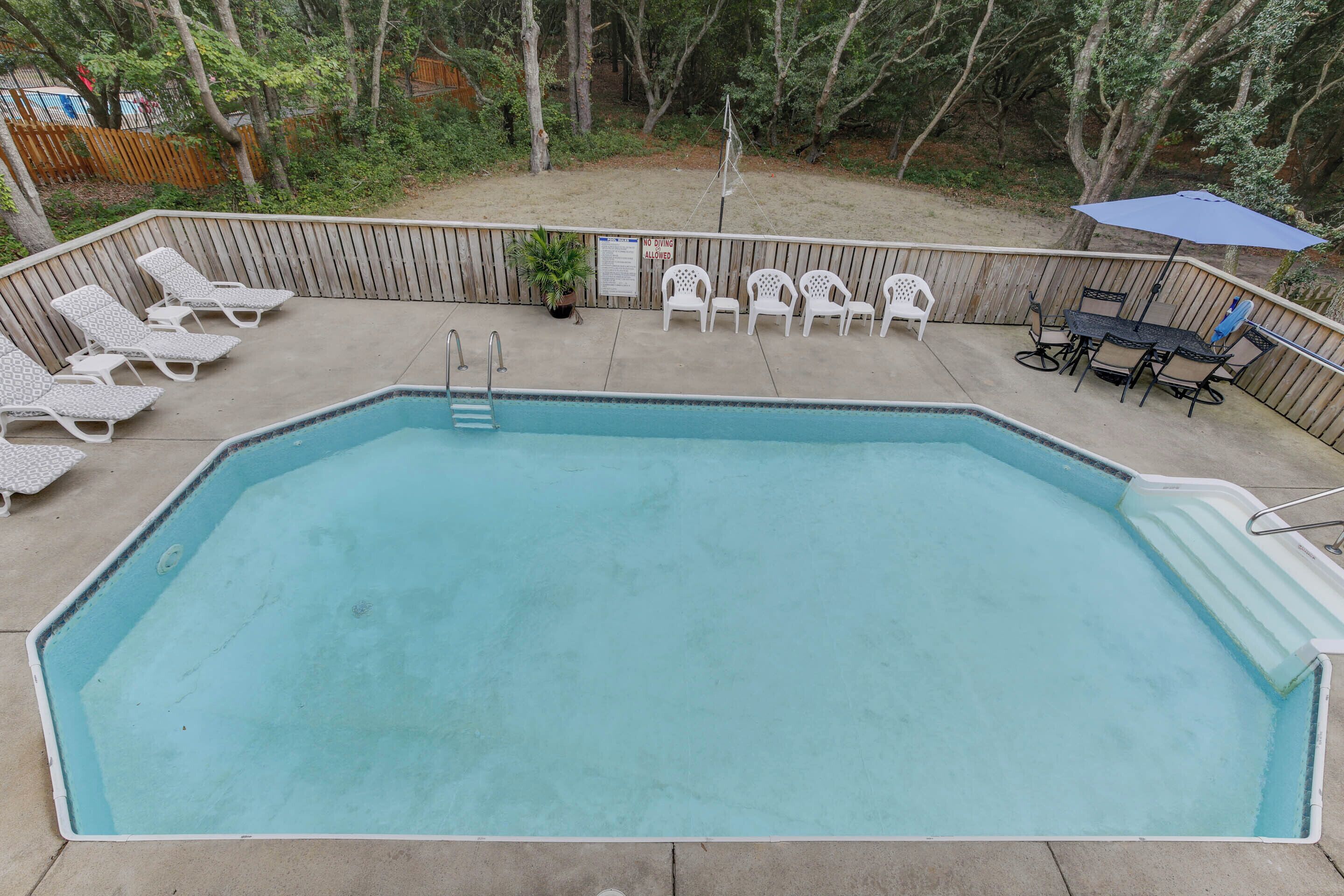 Une piscine rectangulaire hors sol, dotée d’une terrasse en bois, entourée de chaises longues et d’une table avec des chaises.