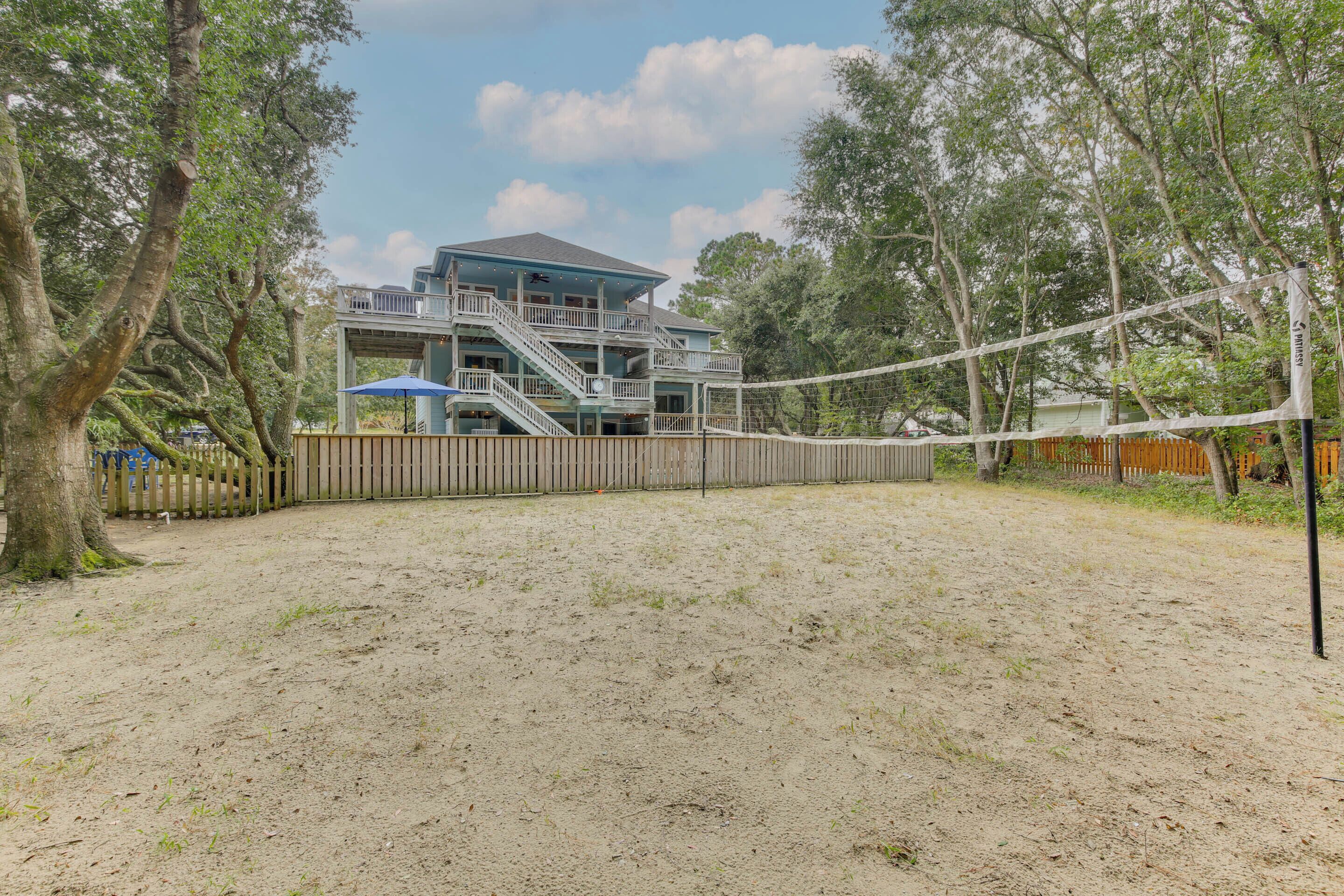 Une maison de plage dotée d’une terrasse en bois, d’un patio couvert et d’un filet de volley-ball.
