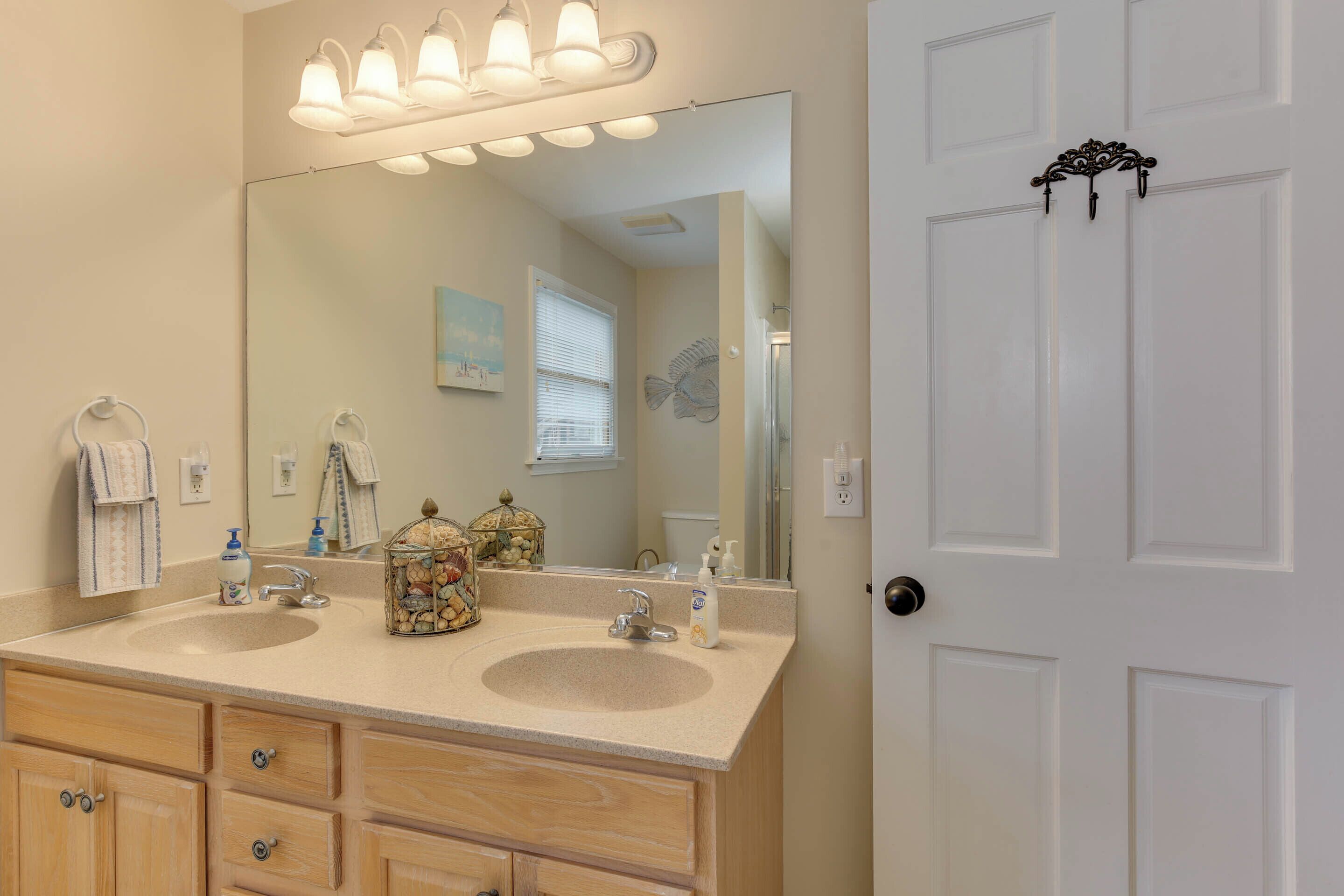 Une salle de bain avec deux lavabos, un grand miroir et une porte dotée d’une poignée décorative.