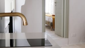 A modern bathroom with a white sink and gold faucet, a mirror, and a view of a bedroom through an arched doorway. - House in the historic center with terrace and panoramic view of the Itria Valley (Locorotondo)