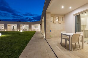 Un espace extérieur aménagé en patio, avec une table et des chaises, une pelouse bien entretenue et un bâtiment comprenant plusieurs pièces.