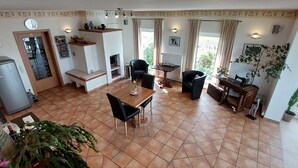 A spacious living area with a tiled floor, a dining table with chairs, a fireplace, and a large window offering a view of greenery.