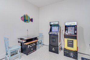 A room with two arcade machines, a Pong table, and a colorful fish decoration on the wall. - Casa de Coconuts by Silver Sands Vacation Rentals (Port Aransas)