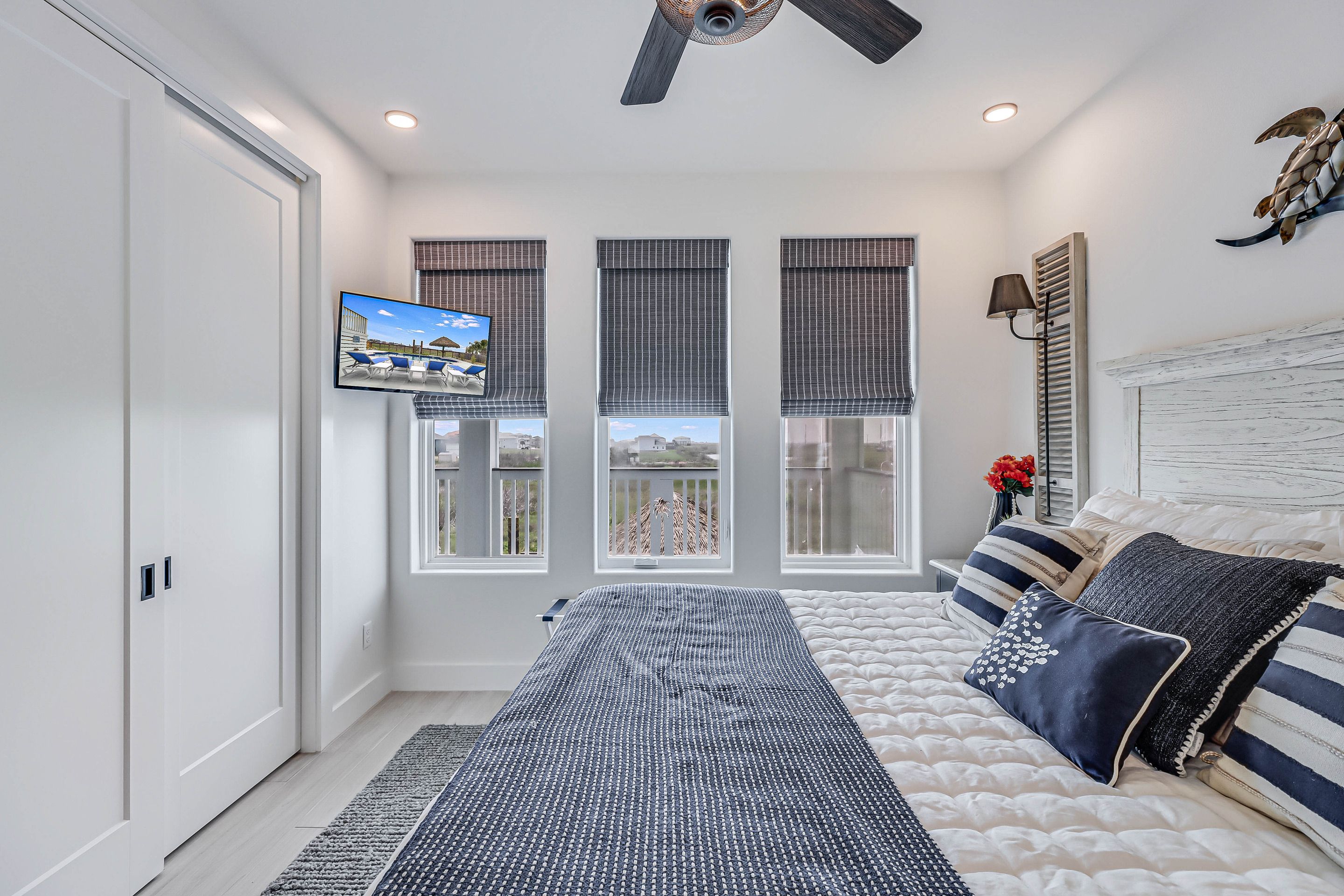 A bedroom with a bed, a TV, and three windows with blinds.