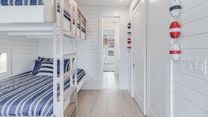 Une chambre avec un lit superposé, une couette à rayures, une échelle en bois et un mur blanc orné de décorations sur le thème de la marine.