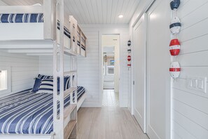 A bunk bed room with a striped bedspread, a wooden ladder, and a white wall with nautical-themed decorations. - Casa de Coconuts by Silver Sands Vacation Rentals (Port Aransas)