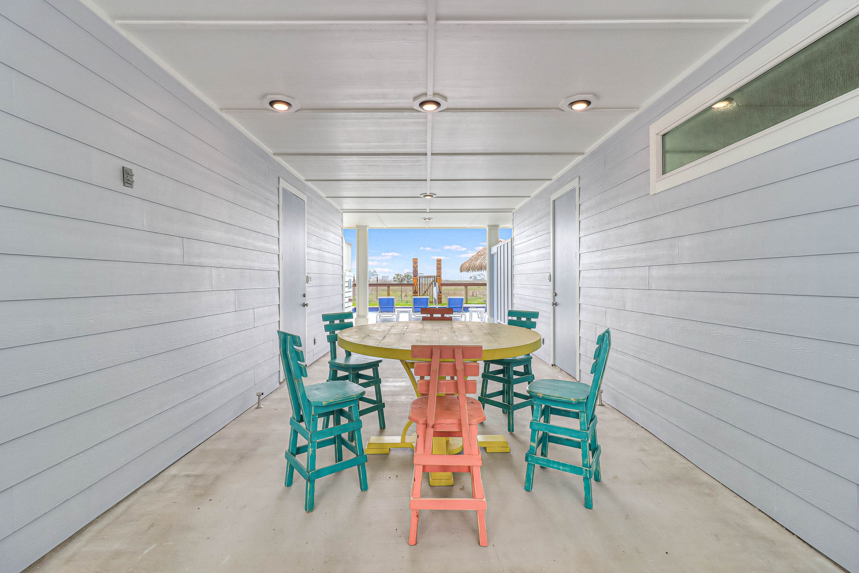 A covered patio with a round table and chairs, white walls, and a view of the beach.