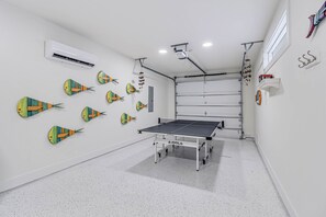 A ping pong table in a room with white walls and a white floor, air conditioning units, and decorative fish wall art. - Casa de Coconuts by Silver Sands Vacation Rentals (Port Aransas)
