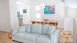 Una sala de estar moderna con un sofá azul claro, una mesa de comedor con sillas, una araña y un cuadro en la pared.