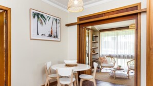 A dining area with a round table and chairs, a framed picture on the wall, and a view into a living room with a sofa and a window. - Harbourview House - coast chic in the CBD (ALBANY)
