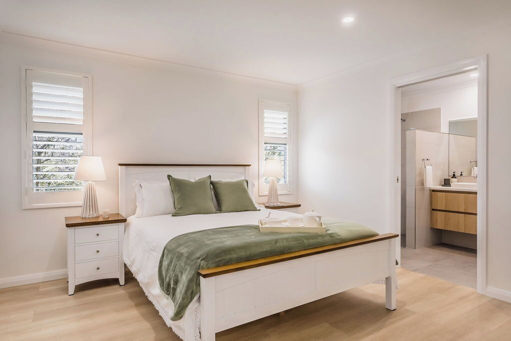 A bedroom with a bed, bedside tables, a nightstand, and a bathroom visible through an open door.