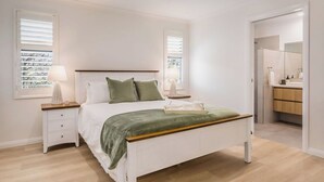 A bedroom with a bed, bedside tables, a nightstand, and a bathroom visible through an open door.