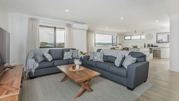 A modern living room with a grey sectional sofa, wooden coffee table, and a view of the kitchen and outdoors.