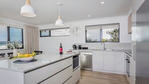 A modern kitchen with white cabinetry, a central island, stainless steel appliances, and a large window providing a view of the outdoors.