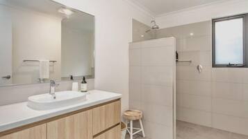 A modern bathroom with a large mirror, two sinks, a shower, and a small stool.