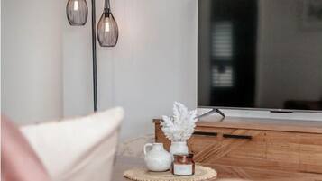 A modern living room with a flat-screen TV, wooden furniture, and decorative items on a wooden table.