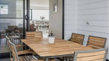 A modern dining area with a wooden table and six chairs, a potted plant, and a view of outdoor seating.