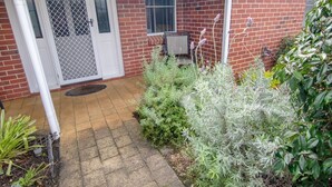 A brick house with a covered patio, a door with a screen, and various plants. - This snug 3 bedroom villa is all you need to call home whilst visiting Albany (MIDDLETON BEACH)
