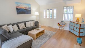 A living room with a grey sofa, a wooden coffee table, a patterned rug, a colorful chair, a blue cabinet, and a painting on the wall. - This snug 3 bedroom villa is all you need to call home whilst visiting Albany (MIDDLETON BEACH)