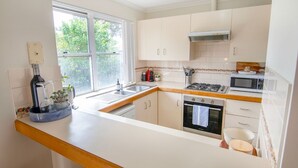 A modern kitchen with white cabinetry, a stainless steel sink, a stove, and a microwave. - This snug 3 bedroom villa is all you need to call home whilst visiting Albany (MIDDLETON BEACH)