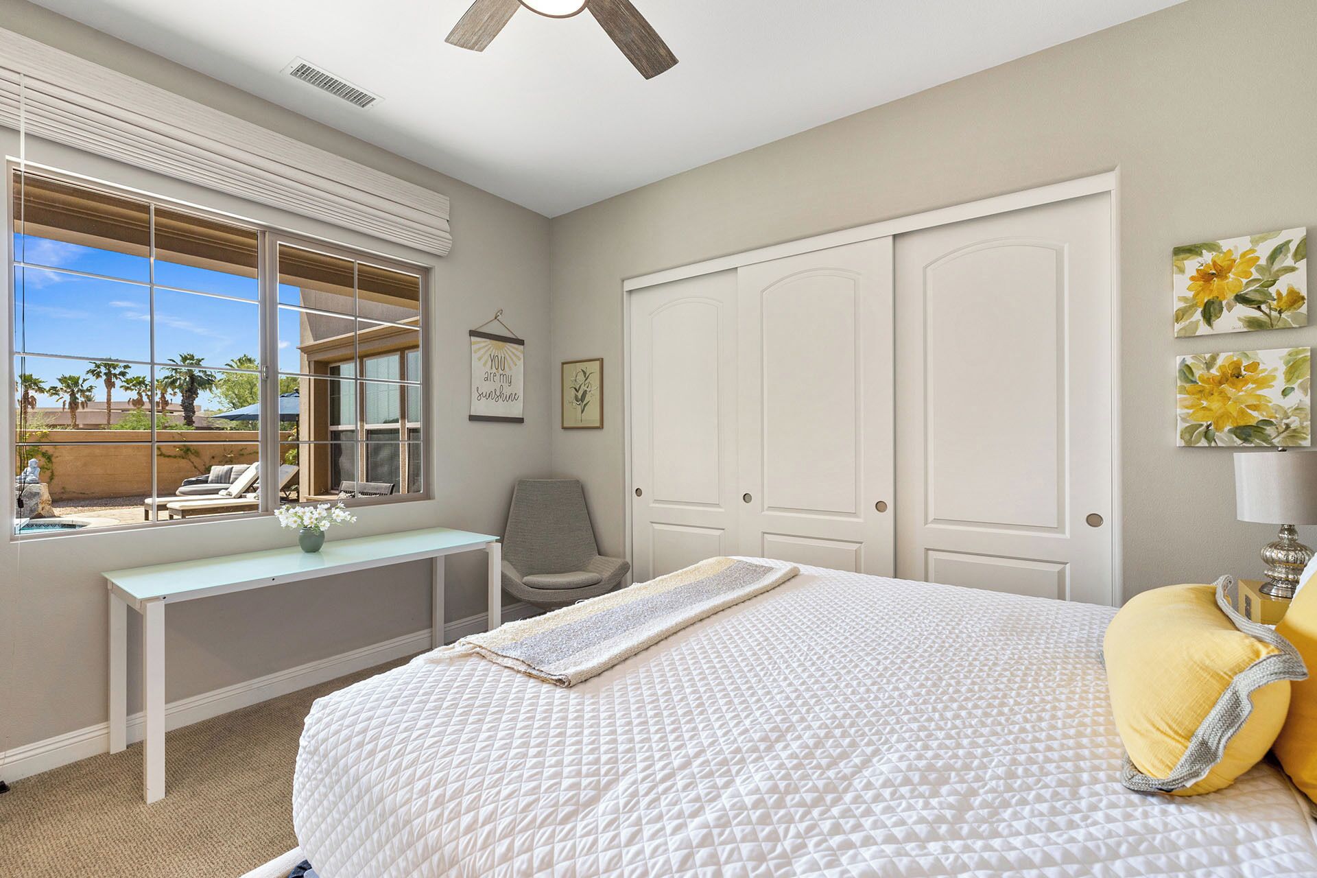 A bedroom with a bed, a desk, a chair, a ceiling fan, and a view of the outdoors.
