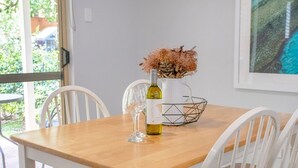 A dining table with white chairs, a wine bottle, and a decorative vase with dried flowers.