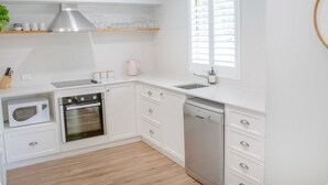 A modern kitchen with white cabinetry, a built-in oven, a dishwasher, and a window with blinds.