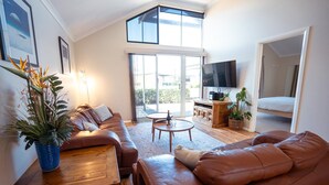 A modern living room with a brown leather sofa, a wooden coffee table, and a large window with a view. - Your summer Beach Escape is calling (ALBANY)