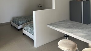 A compact living space with a kitchenette, a bed with patterned bedding, a flat-screen TV, and a refrigerator. - Studio mini (Centonara)