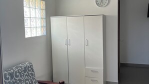 A room with a patterned sofa, a white wardrobe, a wall clock, and an air conditioning unit. - Studio mini (Centonara)
