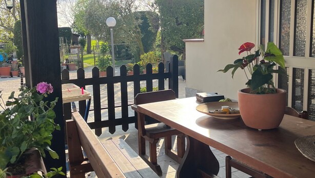 An outdoor patio area with wooden benches and tables, surrounded by potted plants and a white wall. - Studio mini (Centonara)