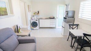 Ein kompakter Wohnraum mit einer Couch, einem Esstisch mit Stühlen, einer Waschmaschine, einer Mikrowelle und einem Kühlschrank.