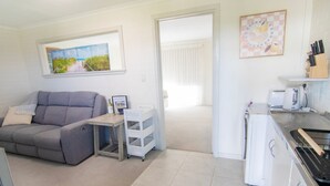 Ein gemütlicher Wohnraum mit grauem Sofa, einem kleinen Esstisch, einer Küchenzeile mit Toaster und Wasserkocher sowie einem gerahmten Bild an der Wand.