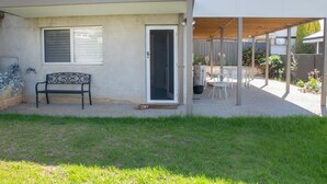Ein überdachter Patio-Bereich mit Bank und Tisch, umgeben von einer Umzäunung und Grünpflanzen.