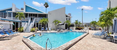 Piscina con sillas de descanso y un edificio de fachada azul.