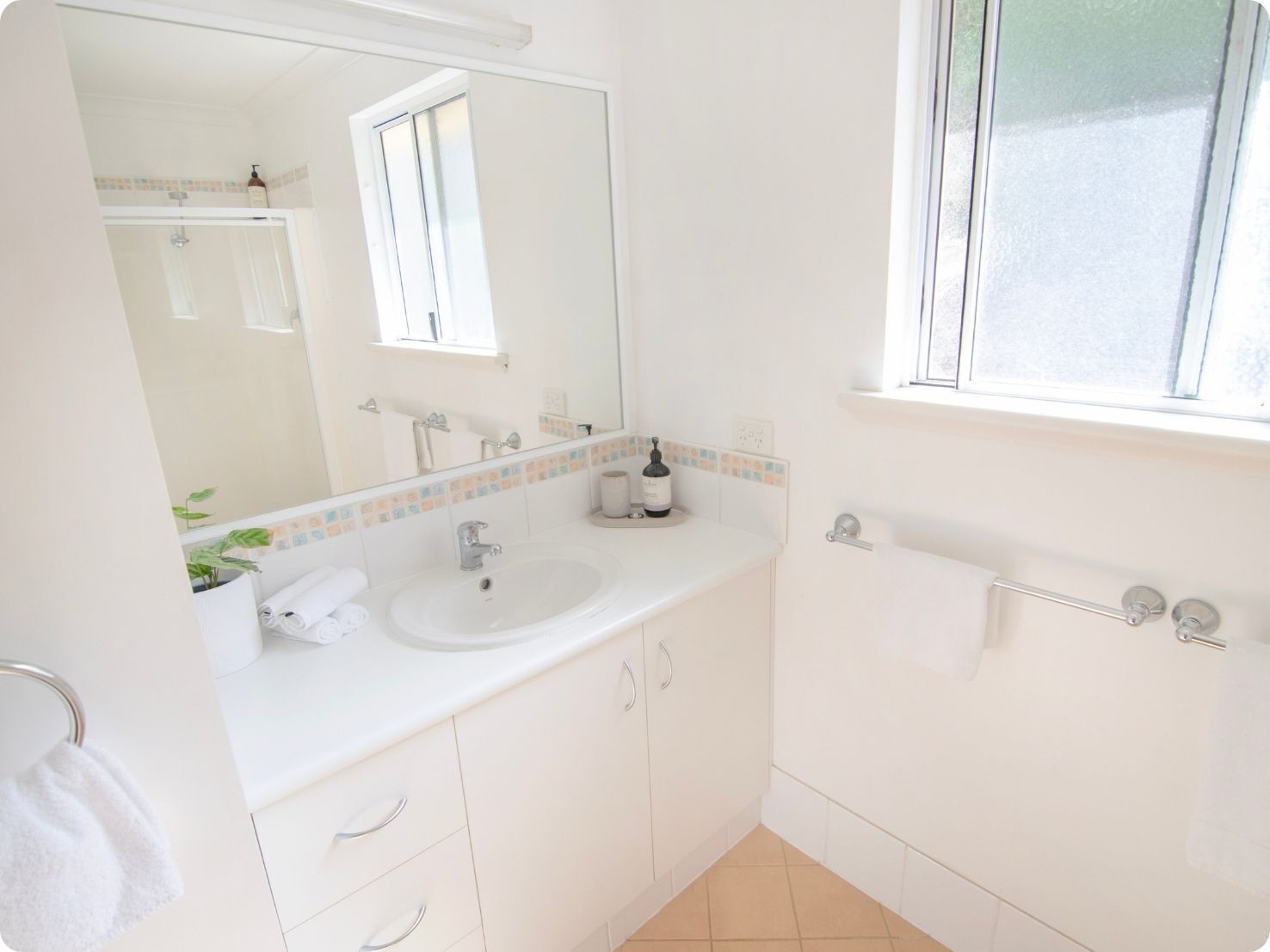 A clean, white bathroom with a sink, mirror, and window.