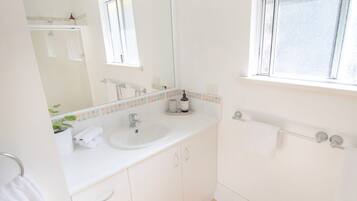 A clean, white bathroom with a sink, mirror, and window.