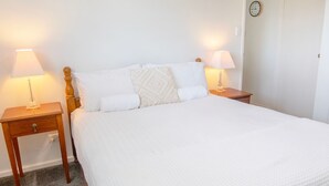 A neatly made bed with white bedding, two bedside tables with lamps, and a clock on the wall. - Cute upstairs 2 bedroom apartment perfect for short stays while visiting Albany (MIRA MAR)