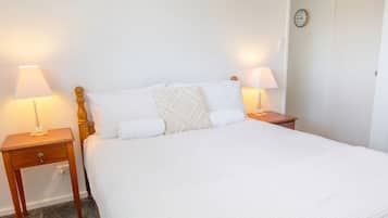 A neatly made bed with white bedding, two bedside tables with lamps, and a clock on the wall.