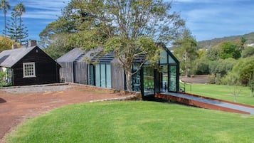 A traditional wooden house with a glass conservatory, surrounded by a well-maintained lawn and trees.