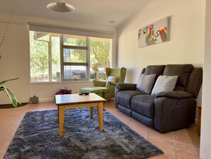 A living room with a large window, a sofa, a green armchair, and a small table. - Light & bright 2 bedroom, 1 bathroom self contained apartment has all you need (ALBANY)