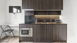 A modern kitchen with dark wood cabinets, a built-in oven, a microwave, a sink, and a toaster. - Executive Apartment (London)